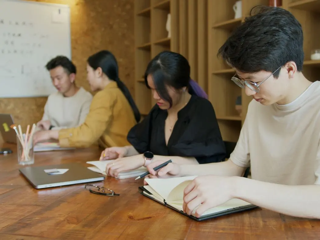 Students working on laptops and notebooks at a long wooden table