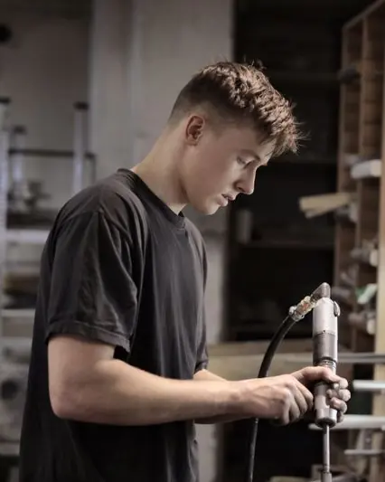 A young man concentrating on a repair at a workshop bench