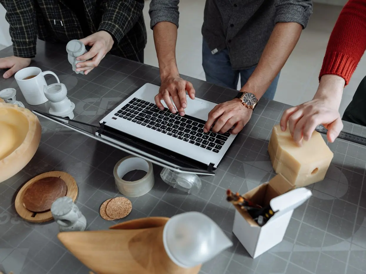 Hands shaping foam product prototypes beside a laptop
