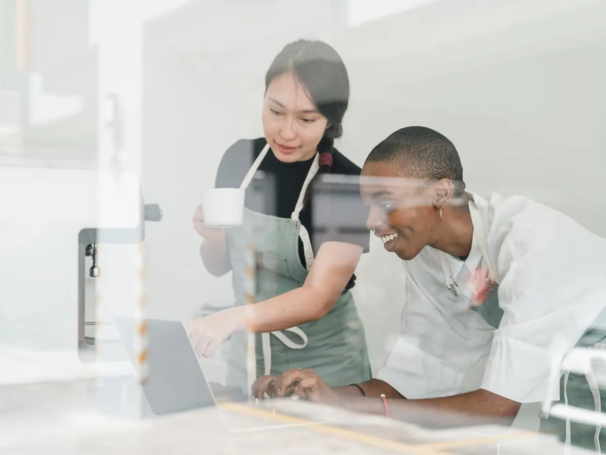 Two young cafe workers checking something on a laptop together