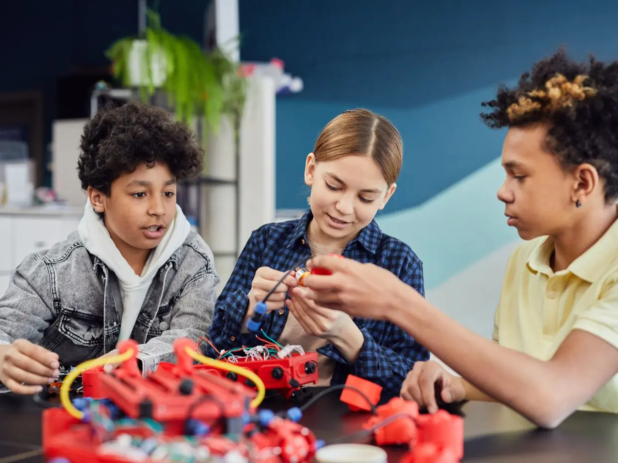 Three teenagers wiring a robotics kit together at a classroom table