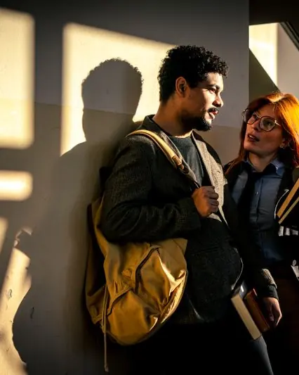 Two students with backpacks talking in a sunlit hallway